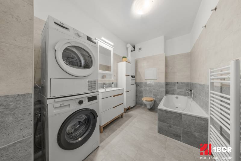 Bathroom of a 2-room apartment with a bathtub, washing machine, and dryer.