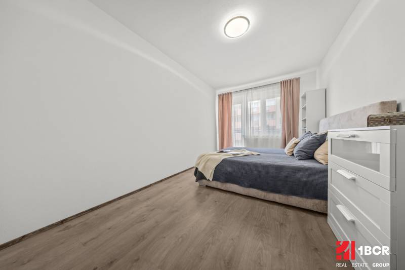 Bright bedroom with a double bed in a 2-room apartment, with wooden flooring and a white dresser.