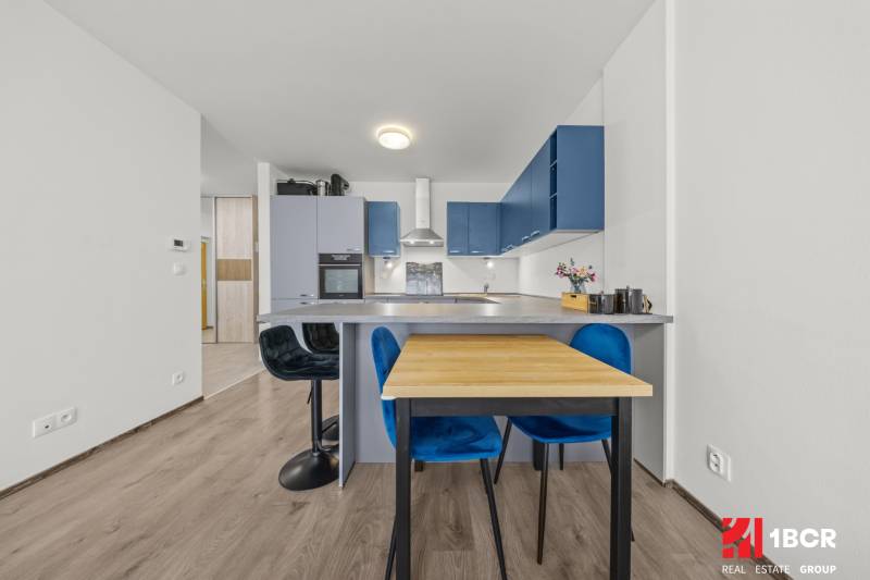 A kitchen in a 2-room apartment with blue cabinets, a dining table, and bar stools.