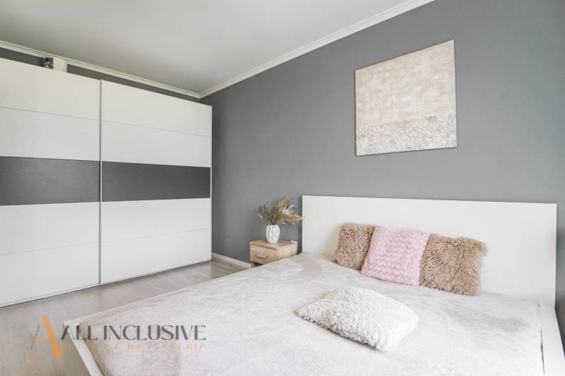 A bedroom in a 2-room apartment with a gray wall, a wardrobe, and decorative pillows.