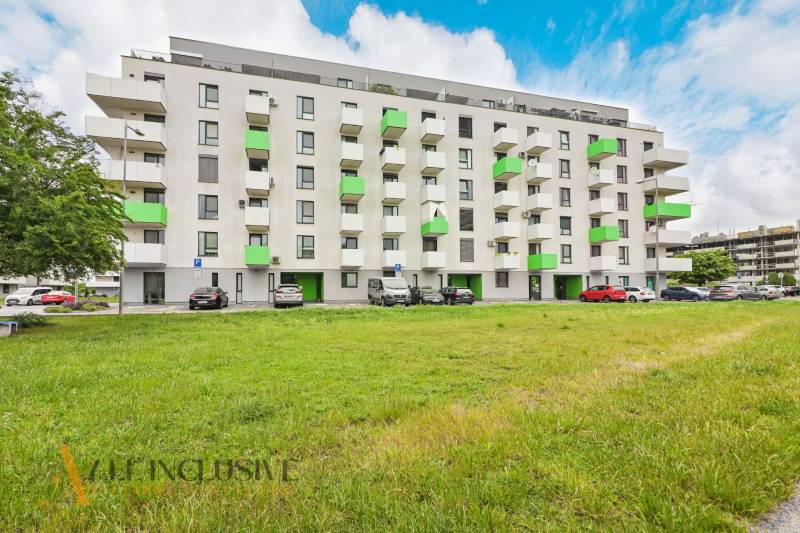 A building with colorful balconies, a parking lot, and greenery in Galanta near Sereď Street.