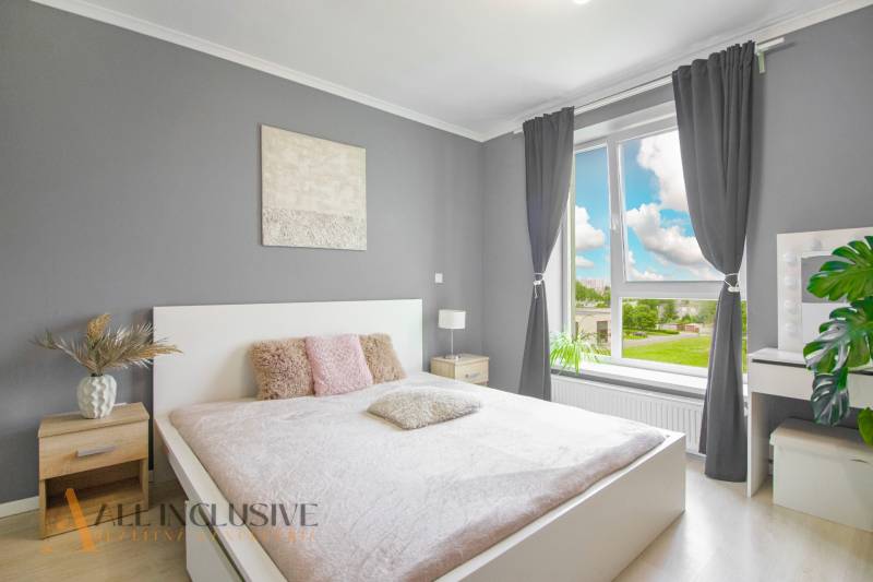 A bright bedroom in a 2-room apartment with a large window and subtle decoration.