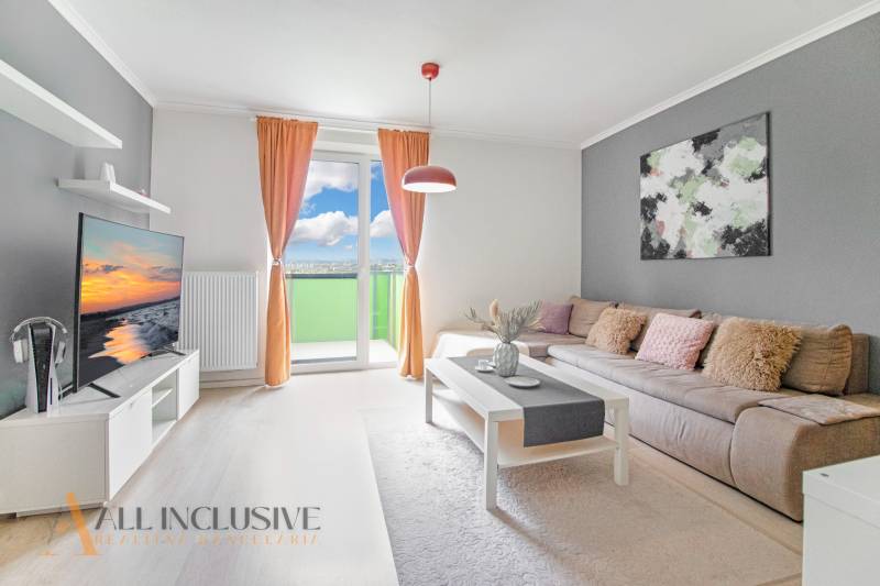 Living room of a two-room apartment with a sofa, television, and balcony, light curtains and accessories.