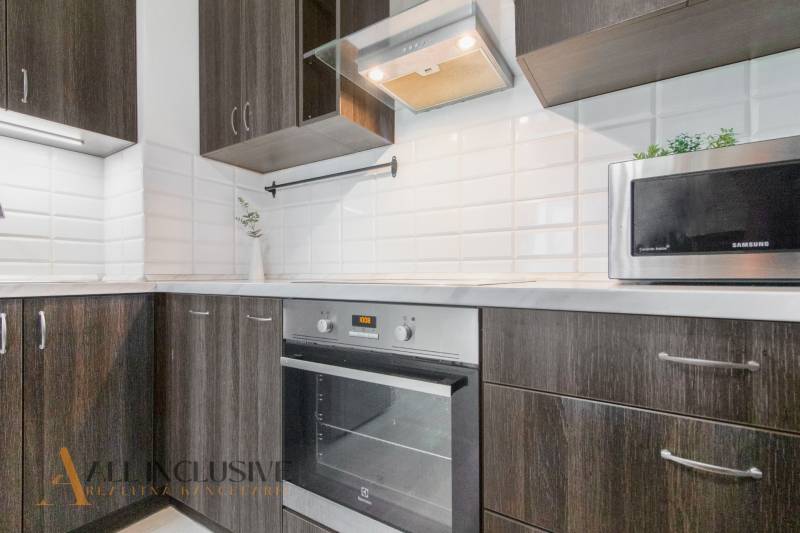 A kitchen in a 2-room apartment with appliances and dark wood, decorated with white tiles.