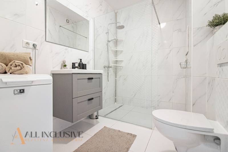 Bathroom in a 2-room apartment with white tiles, a shower, and white furniture.