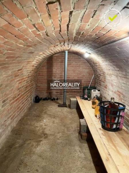 A brick cellar in a cottage with a wooden table and stored bottles.