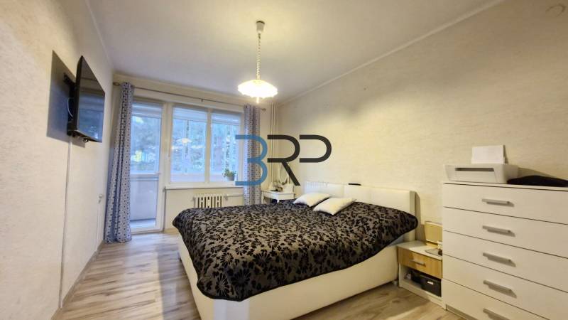 Bedroom in a 3-room apartment with a bed, a TV on the wall, and balcony doors.