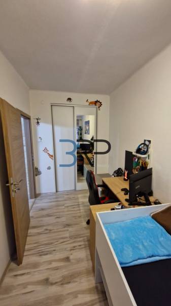 A room with a wooden floor, a workspace, a wardrobe, and a 3-room apartment.