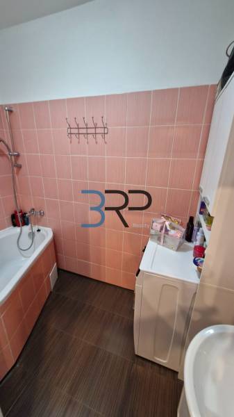 Bathroom with a bathtub and a washing machine, beige tiles, part of a 3-room apartment.