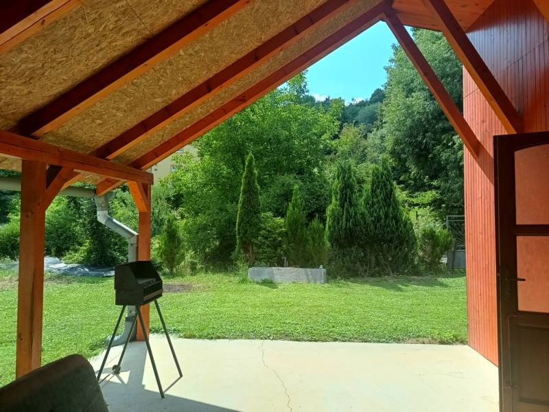 Covered terrace at the cottage in Tužina with a view of the green lawn and trees.