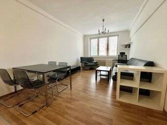 Living room in a two-room apartment with a dining table and a sofa on a wooden floor.