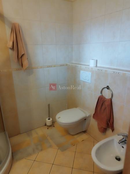 A bathroom in a family house with a shower, toilet, and bidet, with beige tiles.