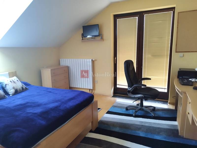 A bedroom in a family house with a bed, a desk, and a door to the balcony.