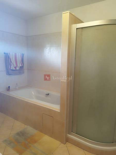 A bathroom in a family house with a bathtub and a shower, tiles in beige tones.