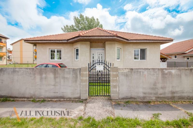 A family house in Selice with a red roof behind a concrete fence and a green yard.
