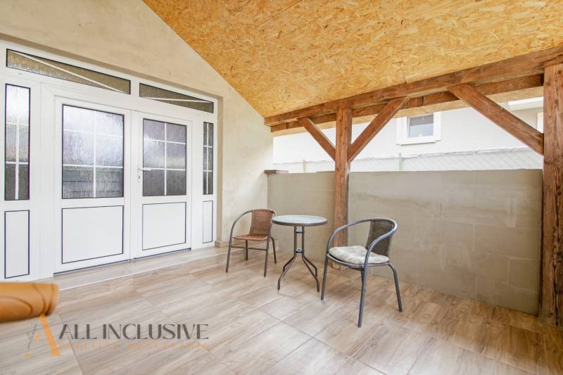 A covered terrace in a family house with rattan furniture and glass doors.
