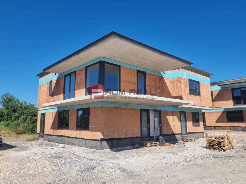 The exterior of an under-construction 3-room apartment in Dubová with brick walls and large windows.