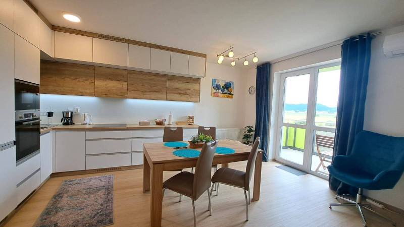 Studio apartment with a bright kitchen, dining table, and a view from the balcony doors.