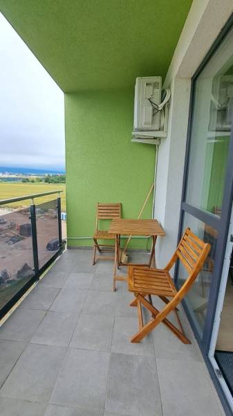 A balcony with a view and wooden furniture in a studio apartment. Green wall, air conditioning.