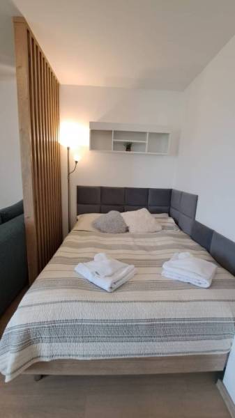 Studio apartment with a bed, wooden partition, floor lamp, and wall shelf with decorations.
