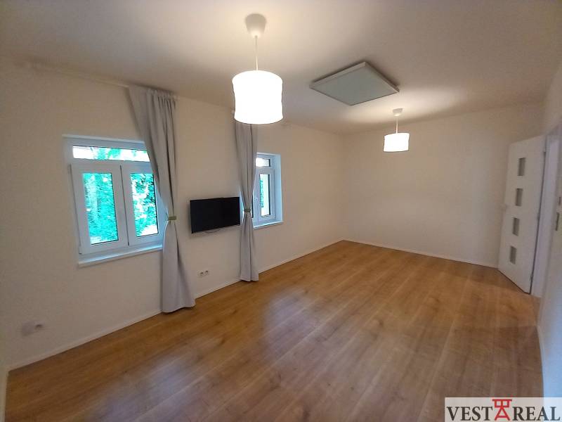 A room in a family house with a wooden floor, a television, and curtains on the windows.