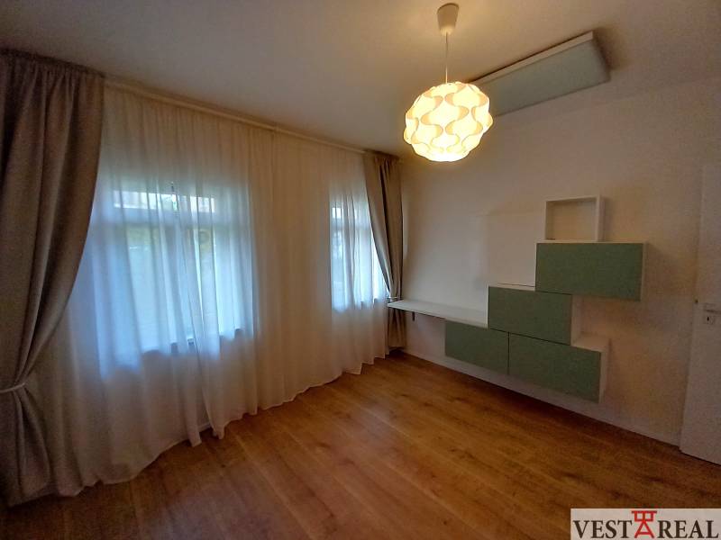 A room in a family house with laminate flooring, curtains, and wall shelves.