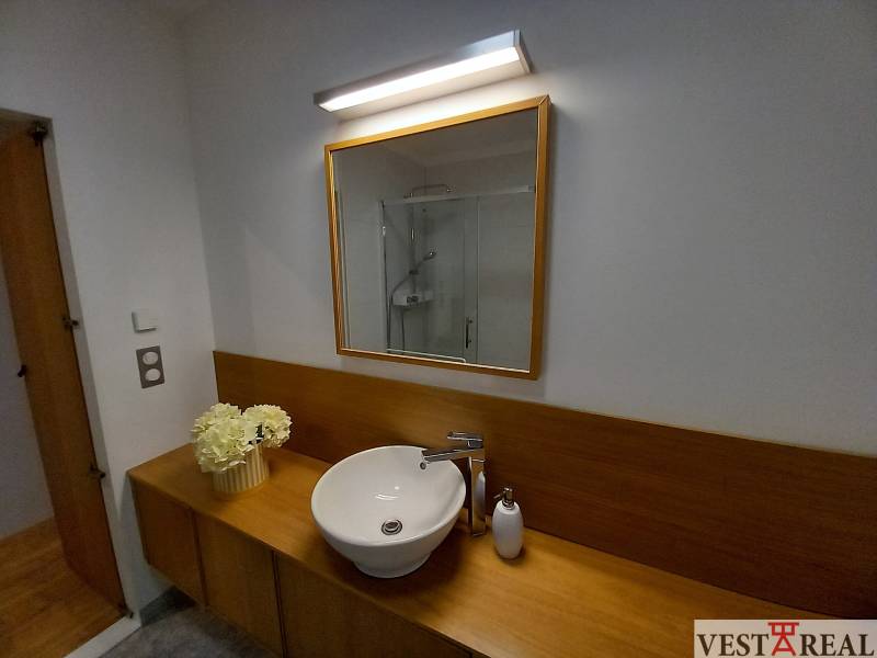 A bathroom in a family house with a sink, mirror, and decorative flowers.