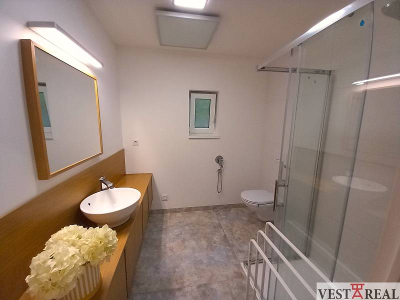 Family house bathroom with a sink, shower, and toilet, decorative flowers on the countertop.