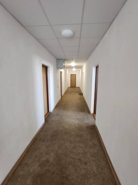 A narrow hallway in a building with white walls and a brown carpet.