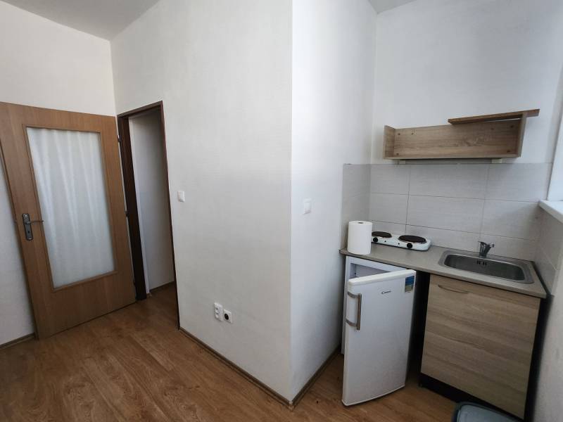 Kitchen in a building with a floor, doors, and small appliances, including a refrigerator and a stove.