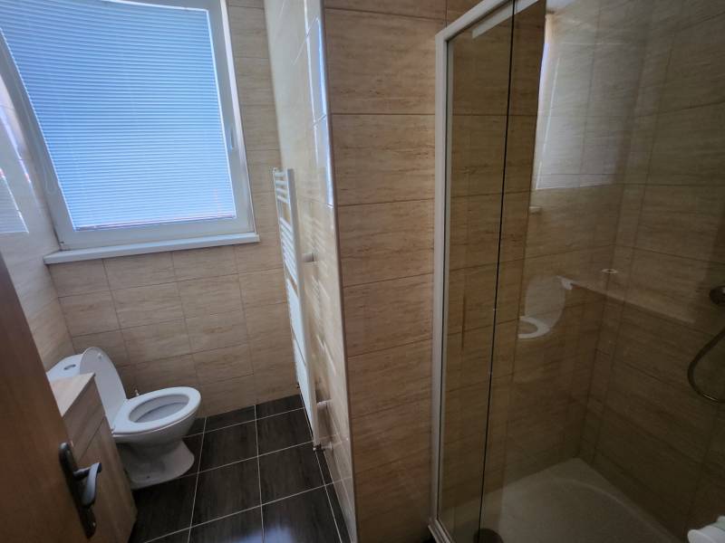 A bathroom in a building with a toilet, shower, and a window with blinds.