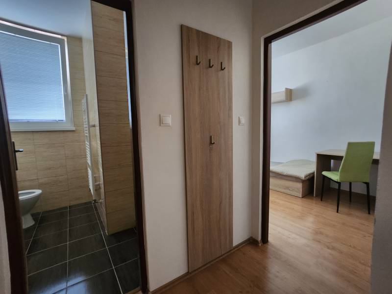 A hallway in a building with doors to a bathroom and a room with furniture.
