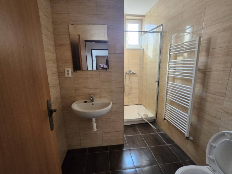 Bathroom in a building with ceramic tiles, a sink, a shower corner, and a ladder radiator.