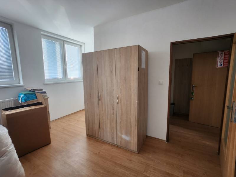 The interior of a building with wooden flooring, a wardrobe, cardboard boxes, and windows with blinds.