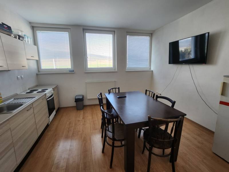 A kitchen with a wooden floor, table, chairs, kitchen unit, stove, and television on the wall.