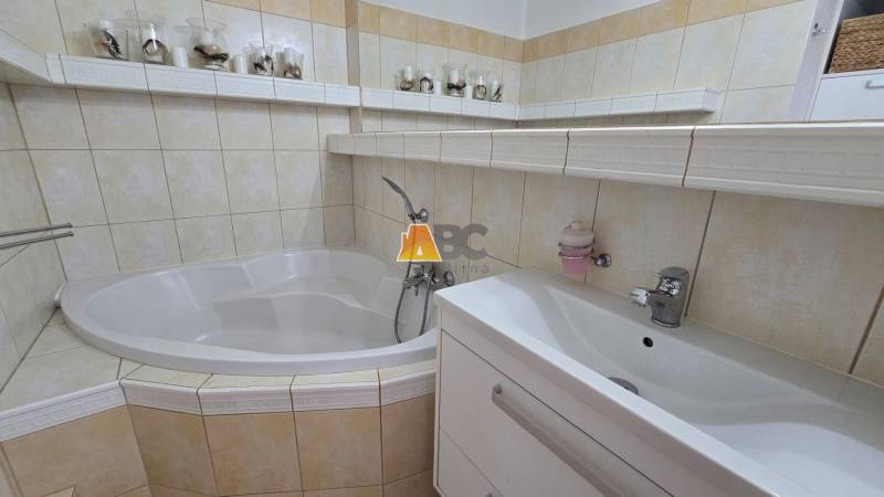 A bathroom in a 2-room apartment with a corner-shaped bathtub and a sink in soft tones.