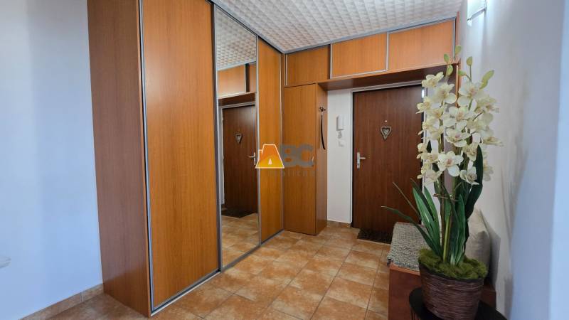 A hallway in a 2-room apartment with wooden cabinets, a mirror, and decorative flowers.