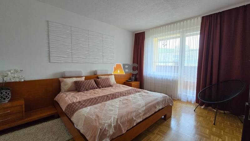 Bedroom in a 2-room apartment with a wooden bed, nightstands, and a large window.
