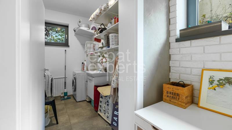 A laundry room in a family house with a sink, washing machine, and shelving storage.
