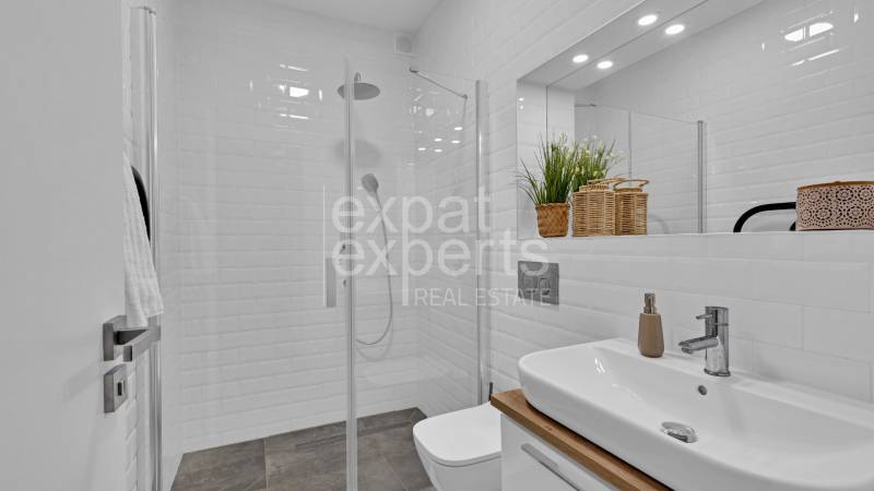 A bathroom with white tiles, a glass shower enclosure, and a sink in a family house.