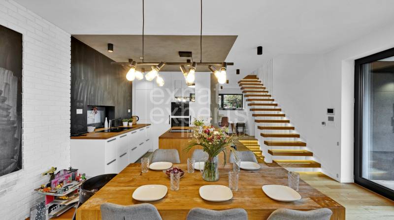 Dining room with kitchen, wooden table, flowers, and staircase in a family house.