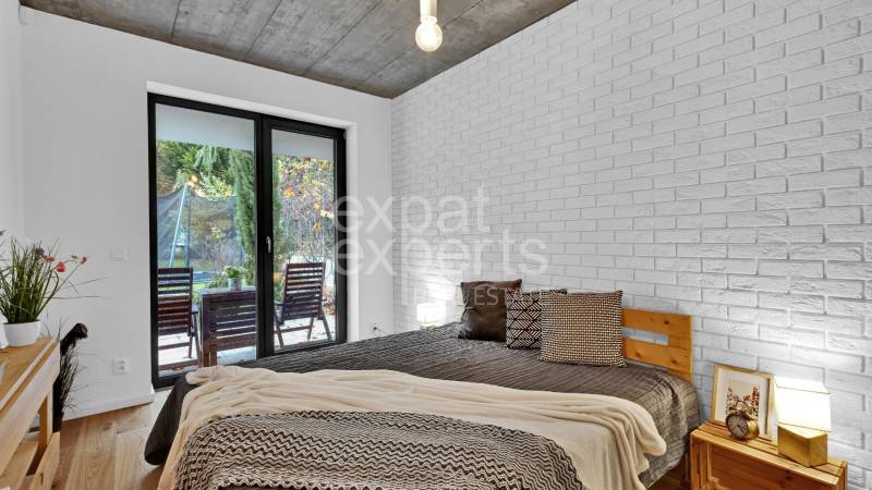 A bedroom in a family house with a bed, a brick wall, and a view of the garden.