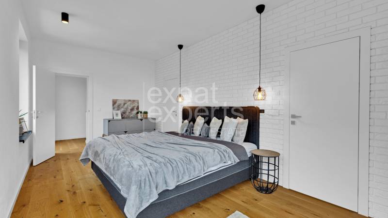 A bedroom in a family house with a wooden floor, a gray bed, and a white brick wall.