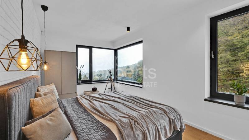 A room in a family house with windows, a bed, a chandelier, and a view of trees.