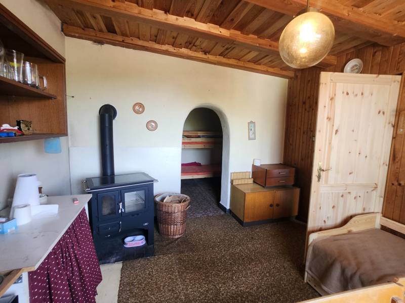 The interior of a cabin with a tiled stove, wooden furniture, and a simple bed.