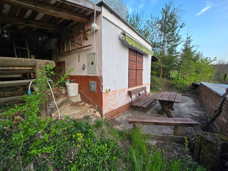 The cottage at Sychrov in Beckov; wooden benches and a table surrounded by greenery and trees.