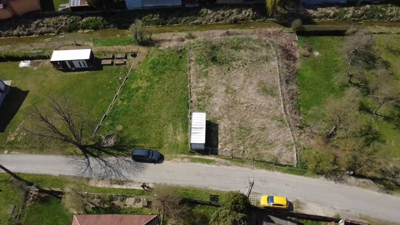 Aerial view of a street with a plot of land, a utility building, and two cars, ideal for living.