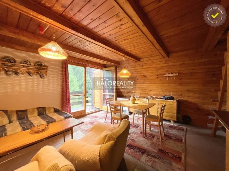 A wooden interior of a cottage with a sofa, a dining table, and glass doors leading to the terrace.