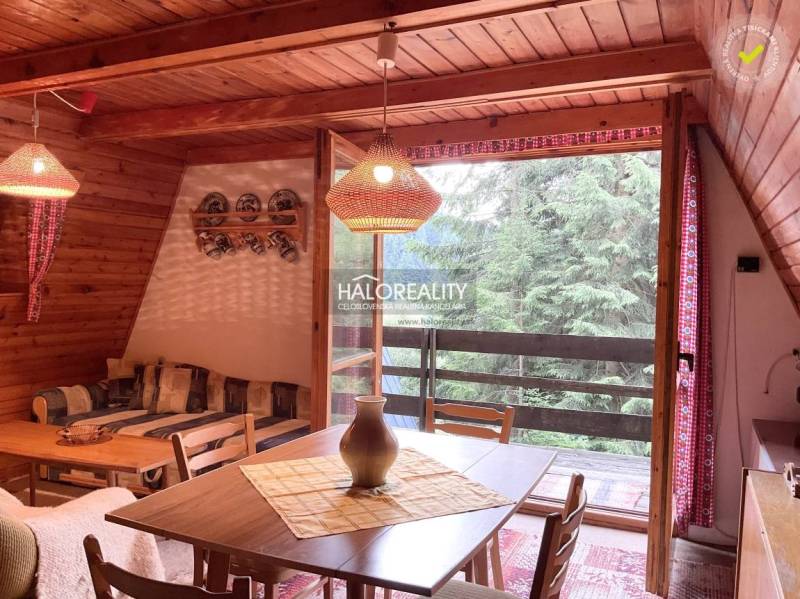 Interior of a cabin with wooden paneling, a dining table, and a view of the forest.