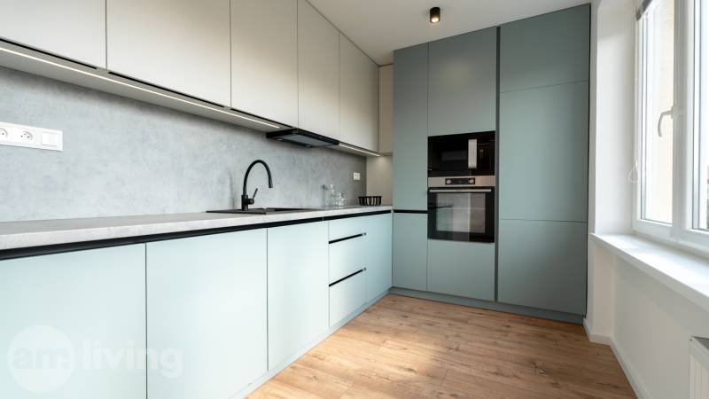 Modern kitchen with pastel cabinets in a 2-room apartment, wooden floor, large window.